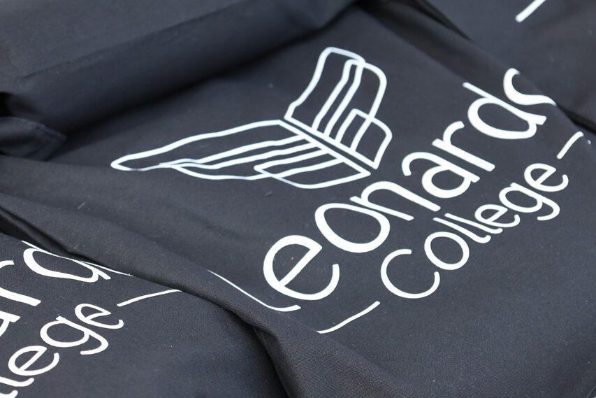 Close-up van opgevouwen zwarte tote bags met het logo en de naam van het Leonardo College